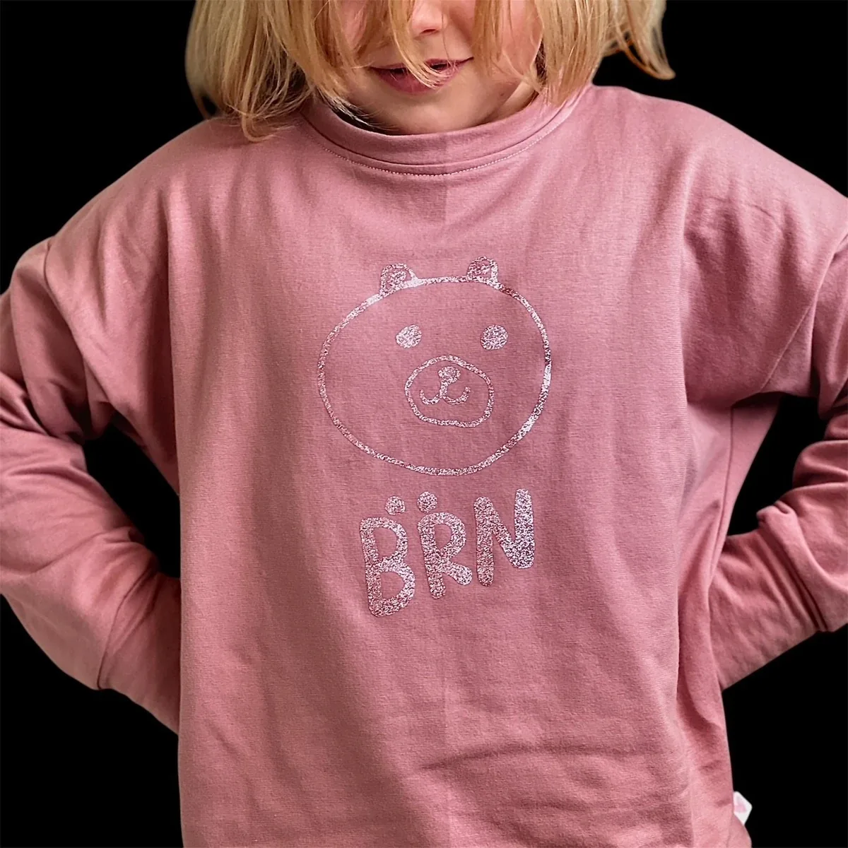 Mädchen in einem altrosa Shirt mit ihrem selbst gezeichneten Bären und Bärn-Schriftzug